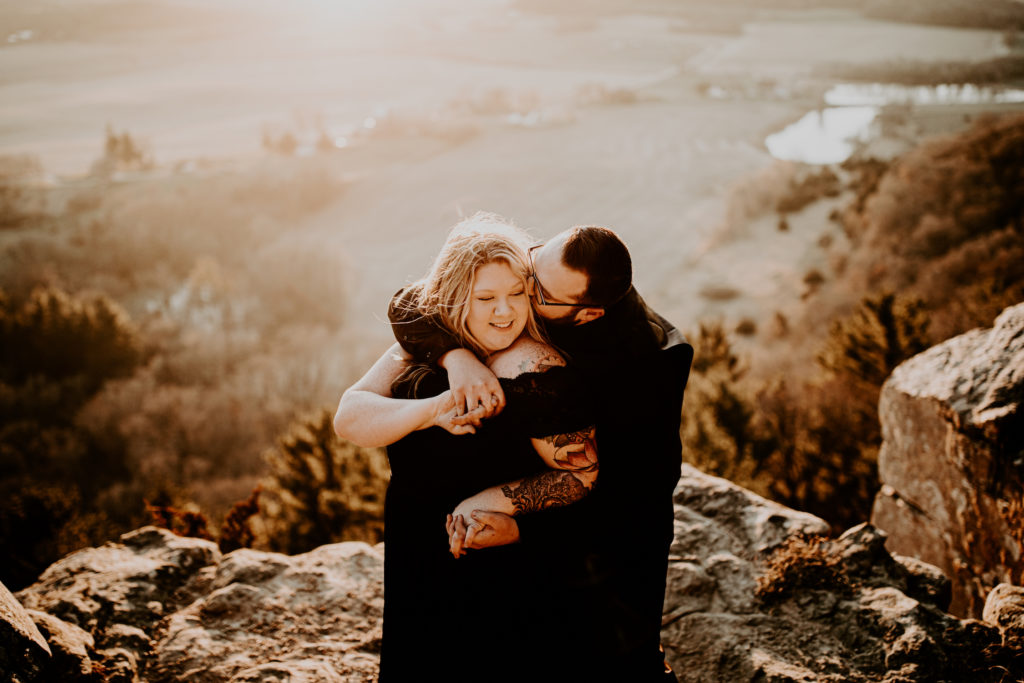 husband with arms around wife on large rock with miles of view while eloping in Wisconsin