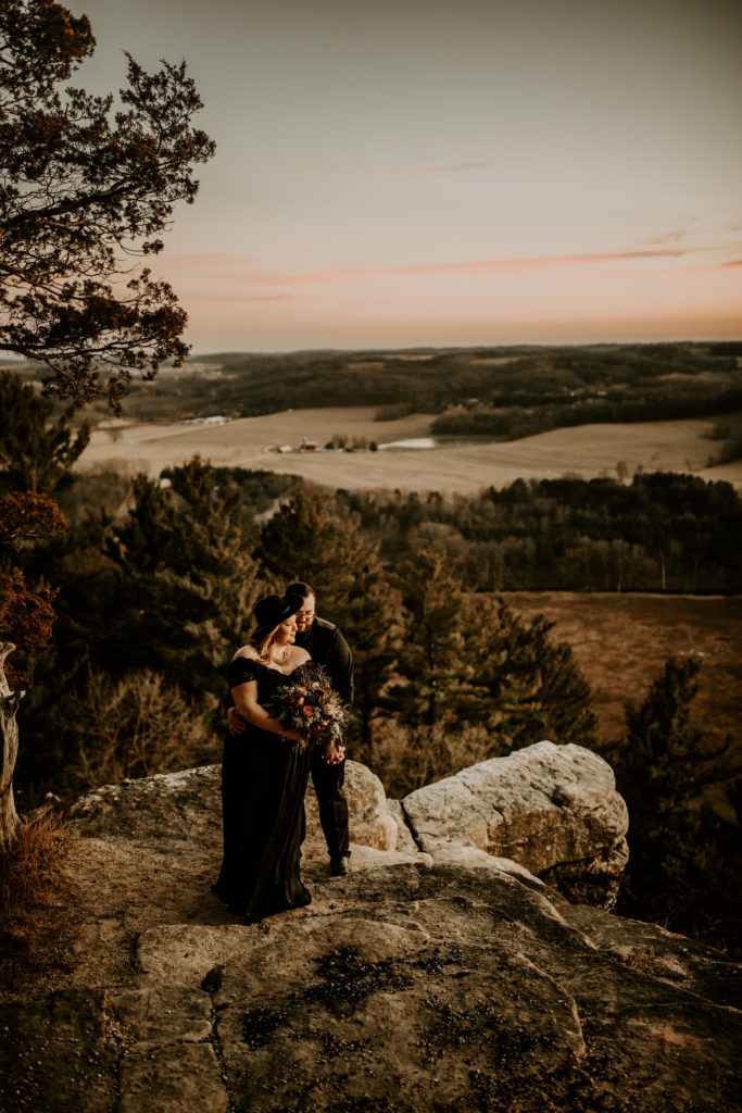 valley view of bride and groom in all black eloping in Wisconsin on top of rock