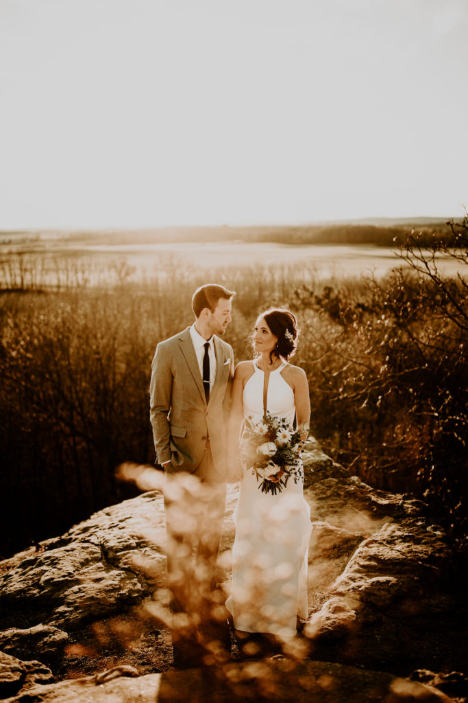 bride and groom standing on rock during sunset photos overlooking field