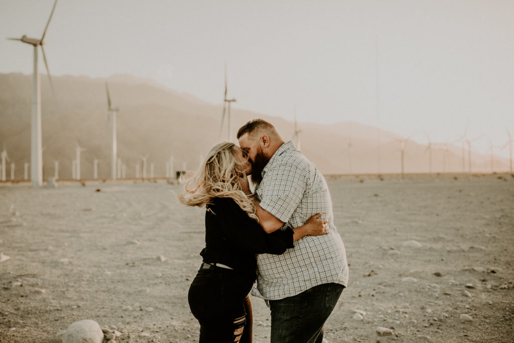 engaged couple taking photos in front of windmills in the desert
