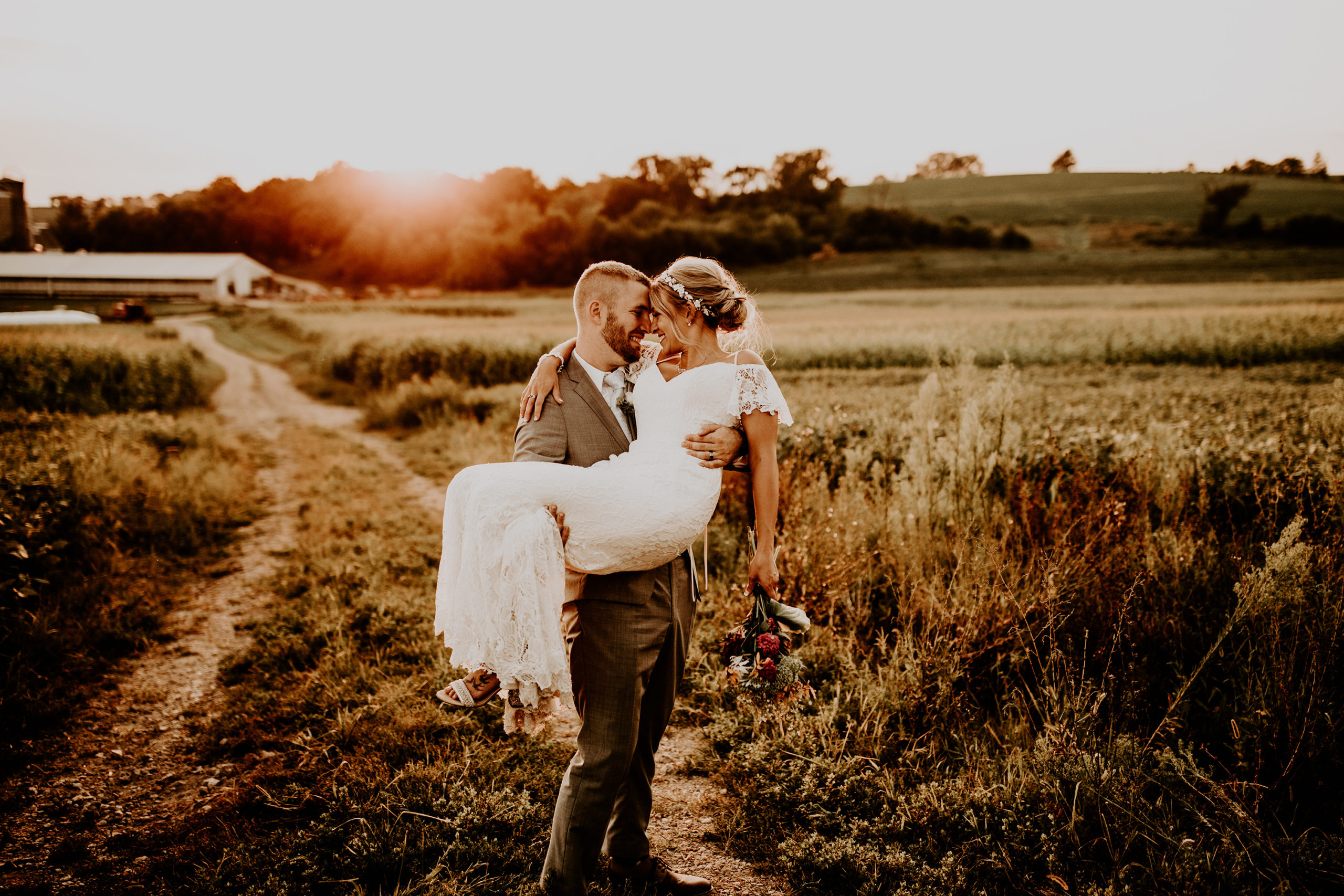 groom holding bride in a farm field