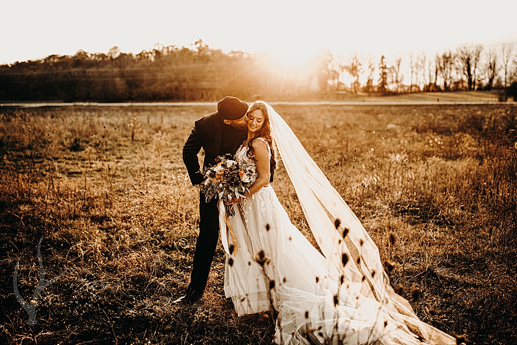 groom kissing bride in long veil in vast field on halloween
