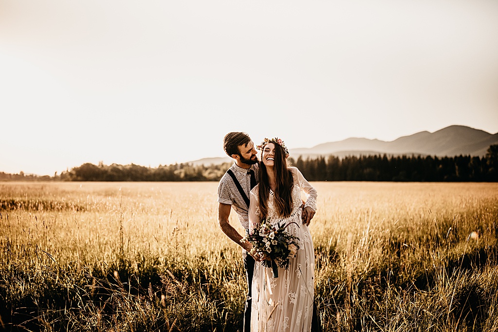 bride and groom laugh in field
