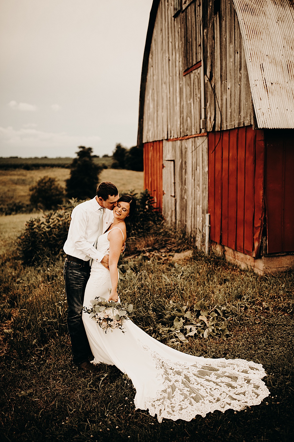 bride and groom kiss in front of a barn