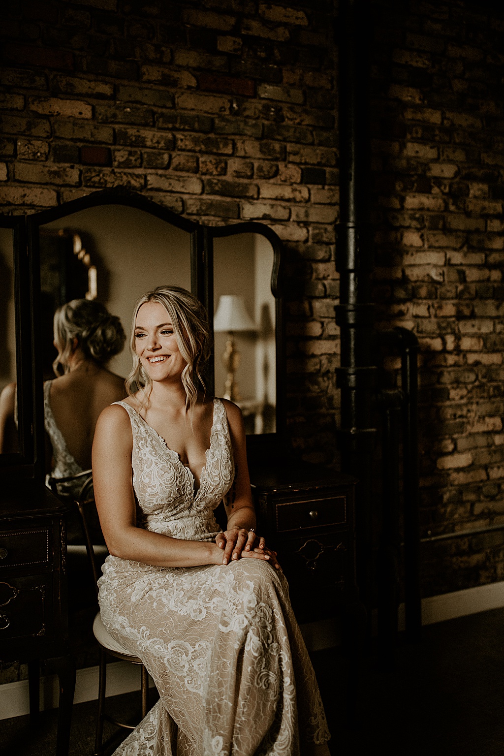 bride in her wedding gown sitting smiling with back against a mirror