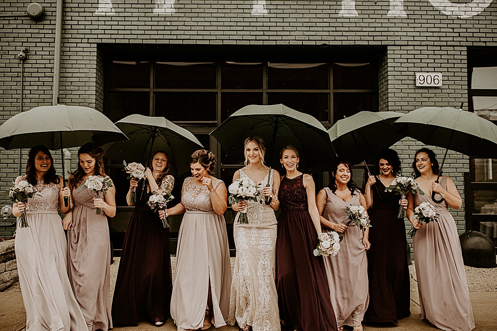 bride with her bridesmaids holding umbrellas outside of venue