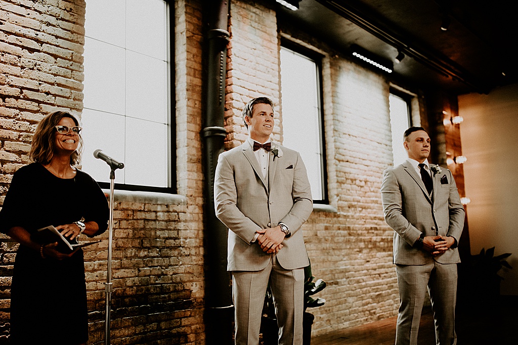 photo of groom smiling while watching bride walk down the aisle