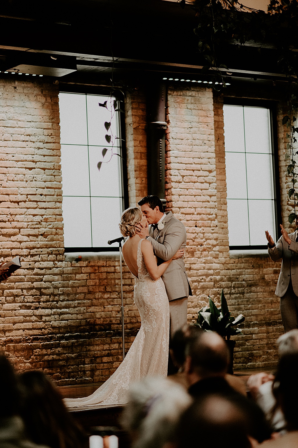 bride and groom kissing at wedding ceremony by large windows in brick building