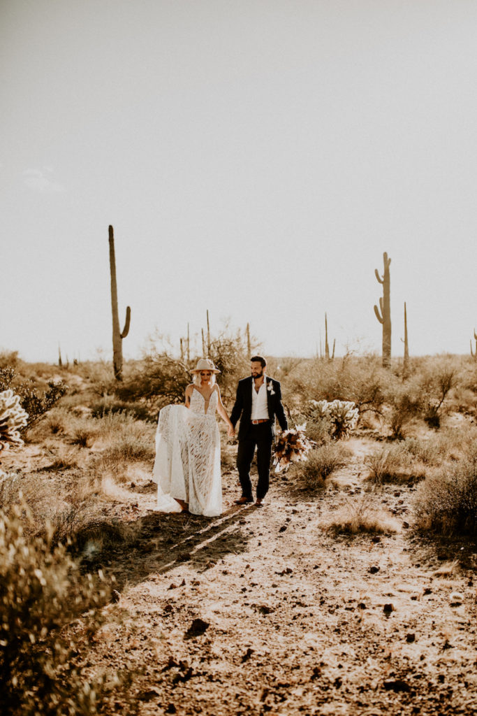 bride and groom holding hands in Arizona desert with cactus in background