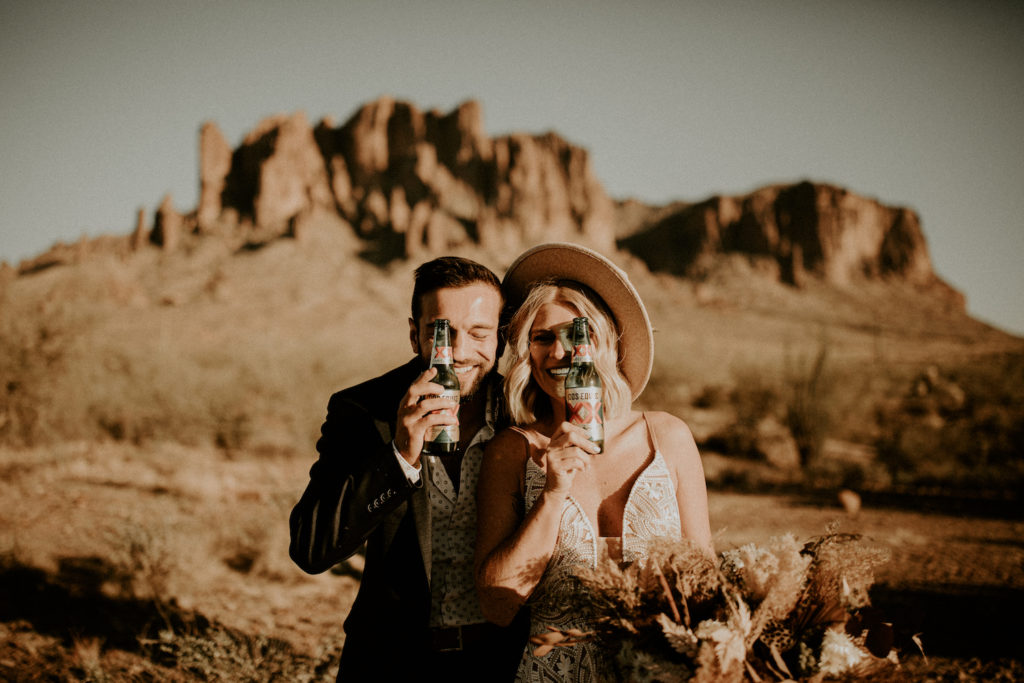 bride and groom by Arizona mountain facing the camera with refreshment bottles in front of face