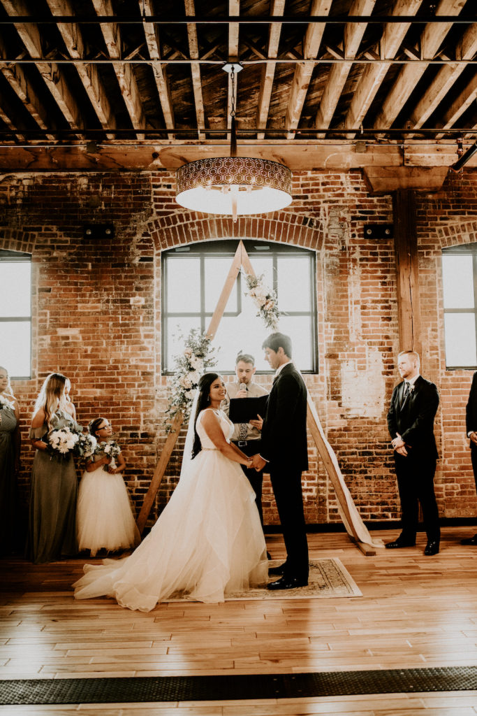 husband and wife standing in front of a triangle alter in a historic building with exposed beams at their ceremony