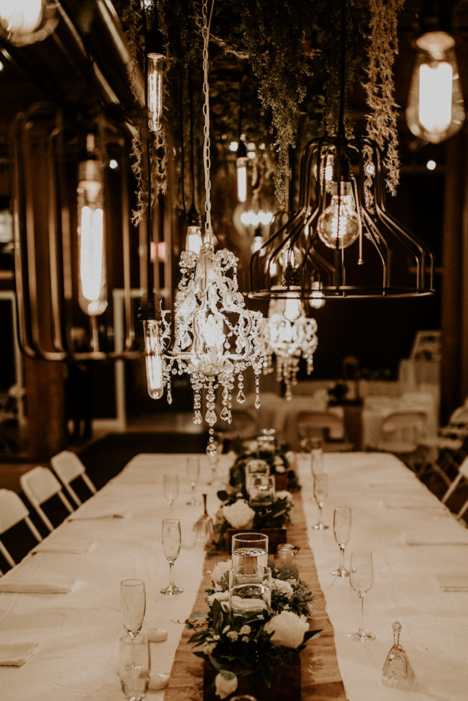 Lit lanterns above table centerpieces at rustic wooden beautiful wedding venue