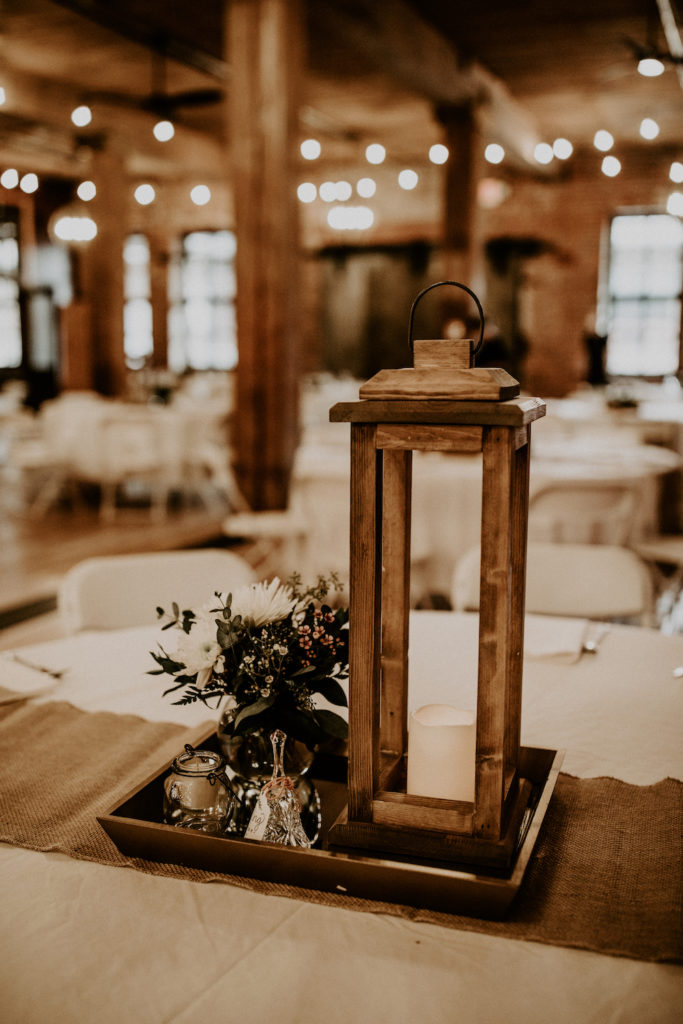 wooden candle lantern on wedding table centerpiece with floral arrangement and burlap across table