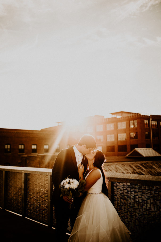 bride and groom kissing at sunset on rooftop with old historic building in background