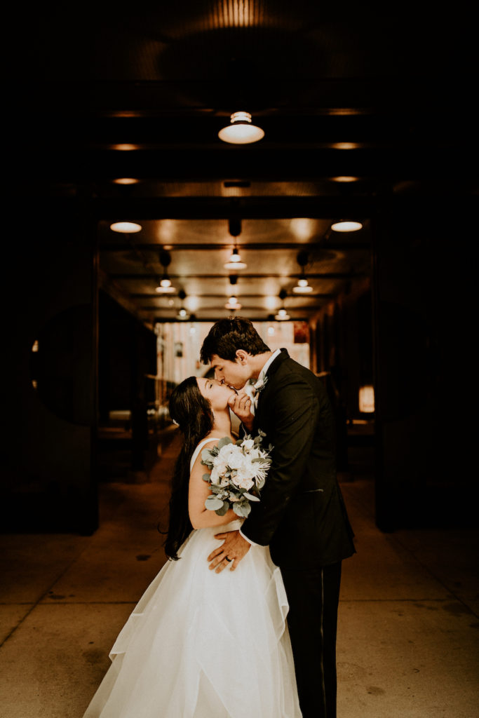 bride and groom kissing in entrance of old building with exposed beams and lights
