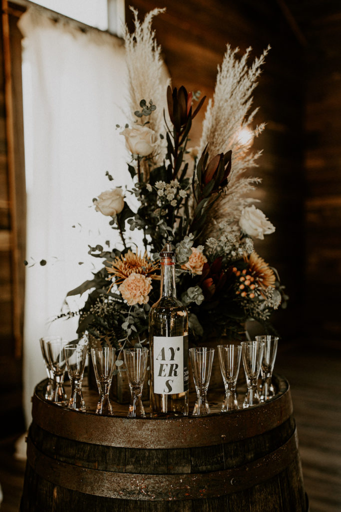 halloween wedding with orange green and tan floral bouquet with wine glasses on whiskey barrel