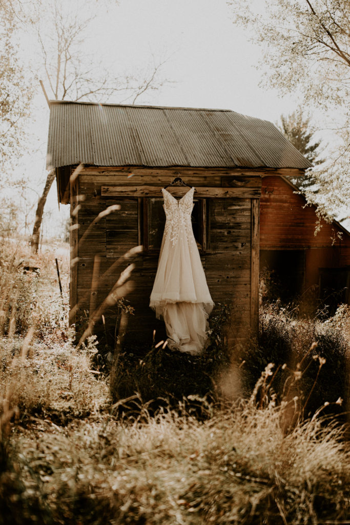 lace wedding dress hanging on old barn building