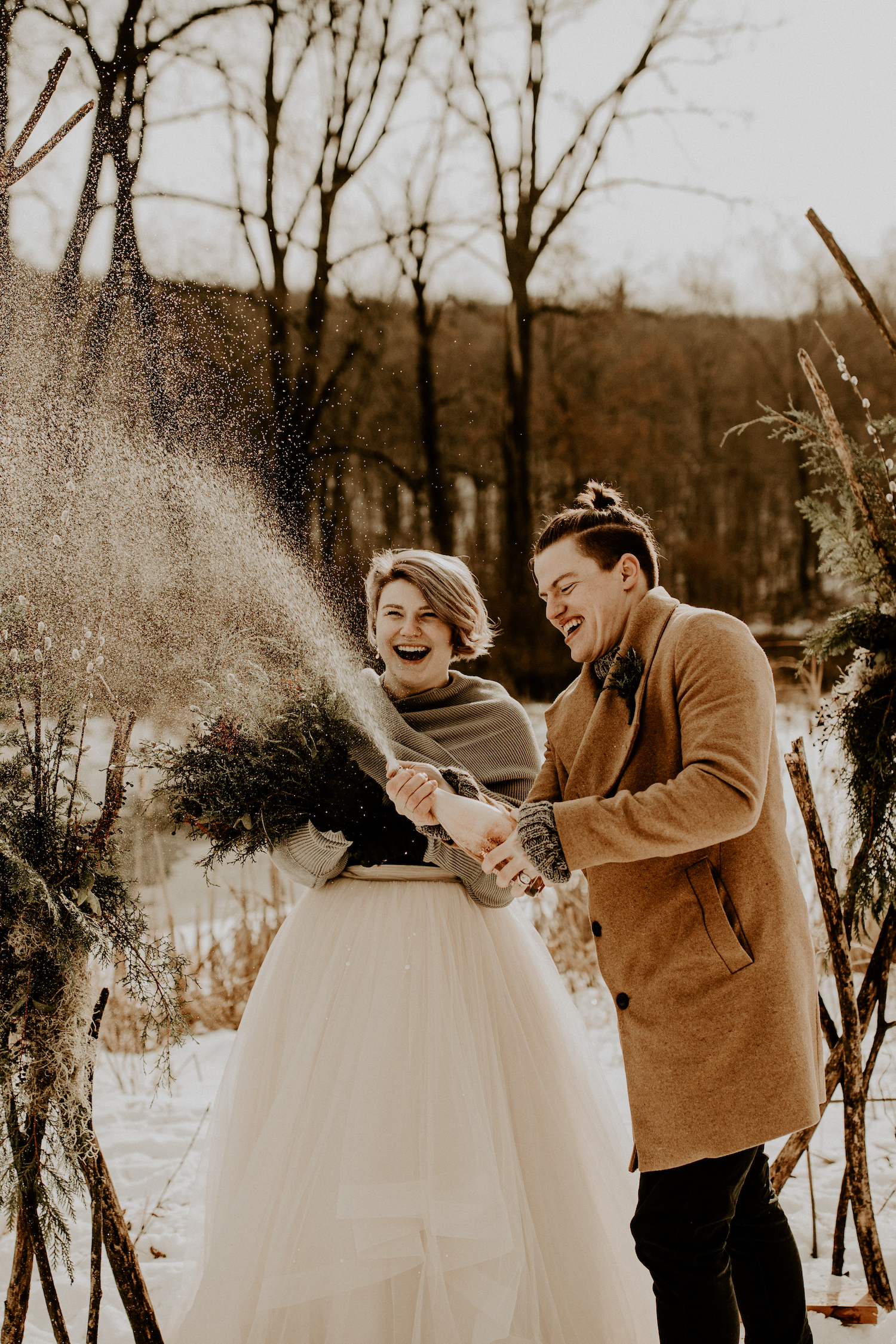 newlywed couple opening bottle of champagne outside in the winter