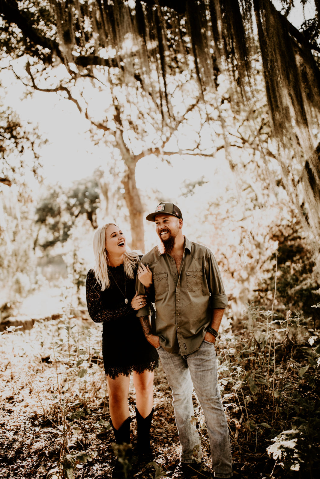 couple walking through Texas Spanish moss during engagement photo shoot