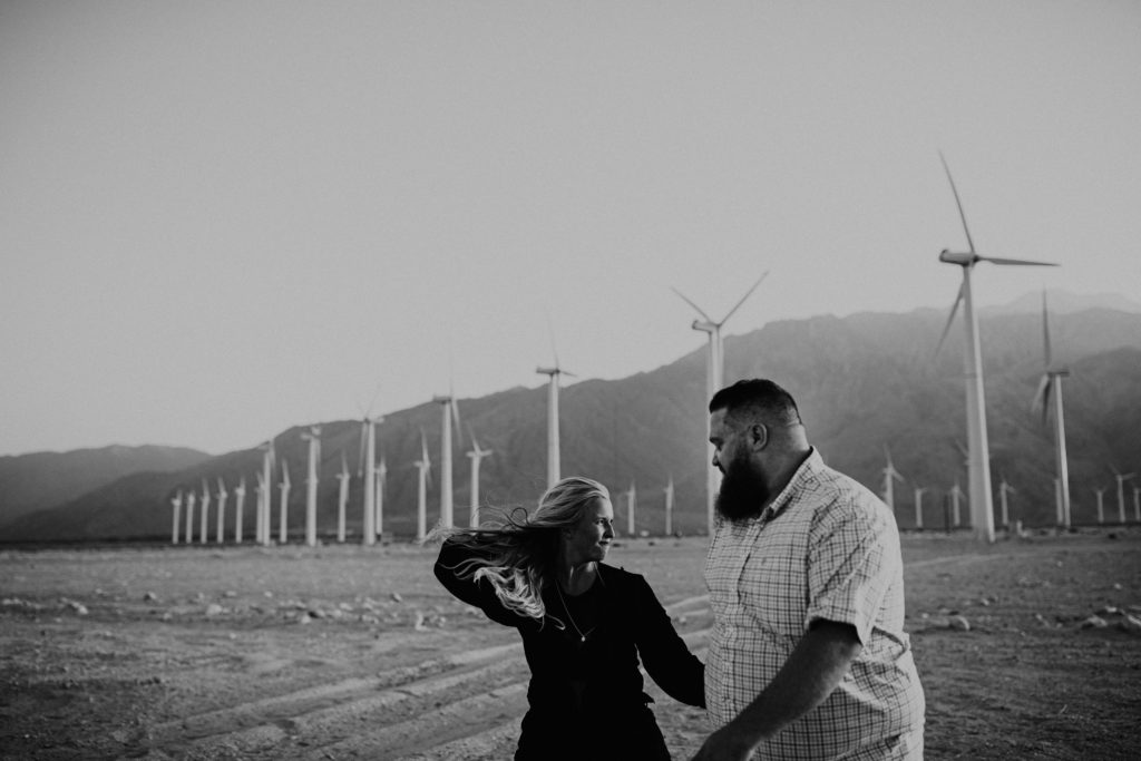 black and white photo of couple near a row of windmills in the desert